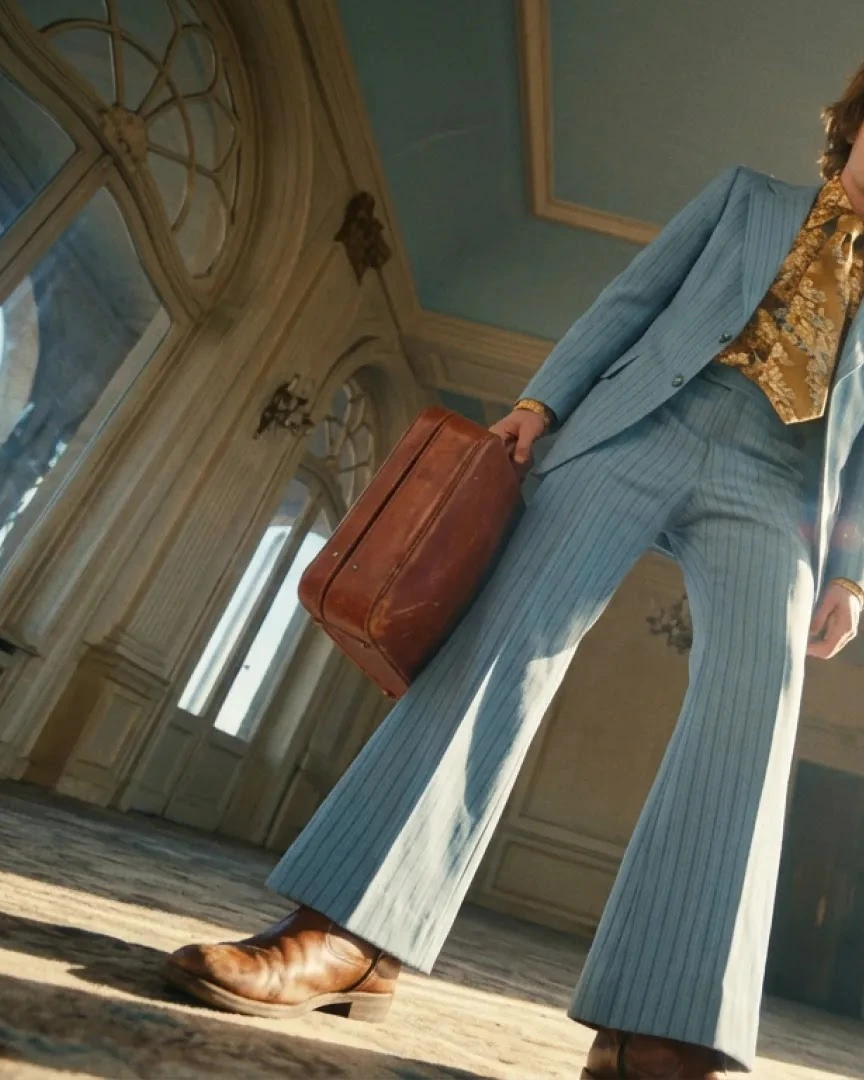 Low-angle retro portrait of a person with a blue suit and leather suitcase